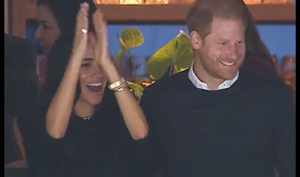 Harry smiles and Meghan claps at ice hockey